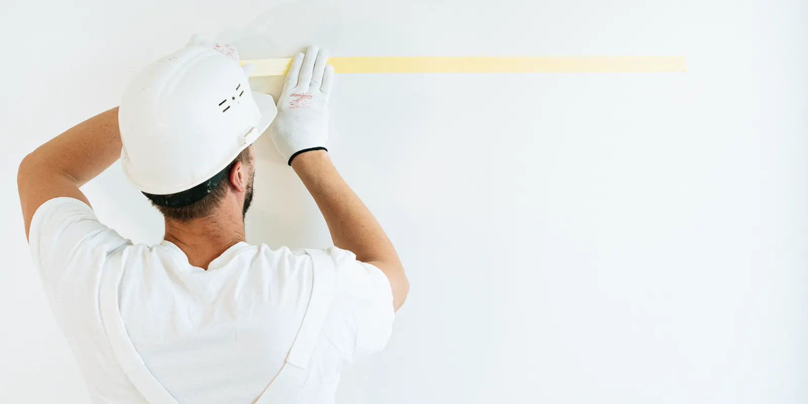 A worker seen from behind applying painter tape to a wall, bathtub reglazing