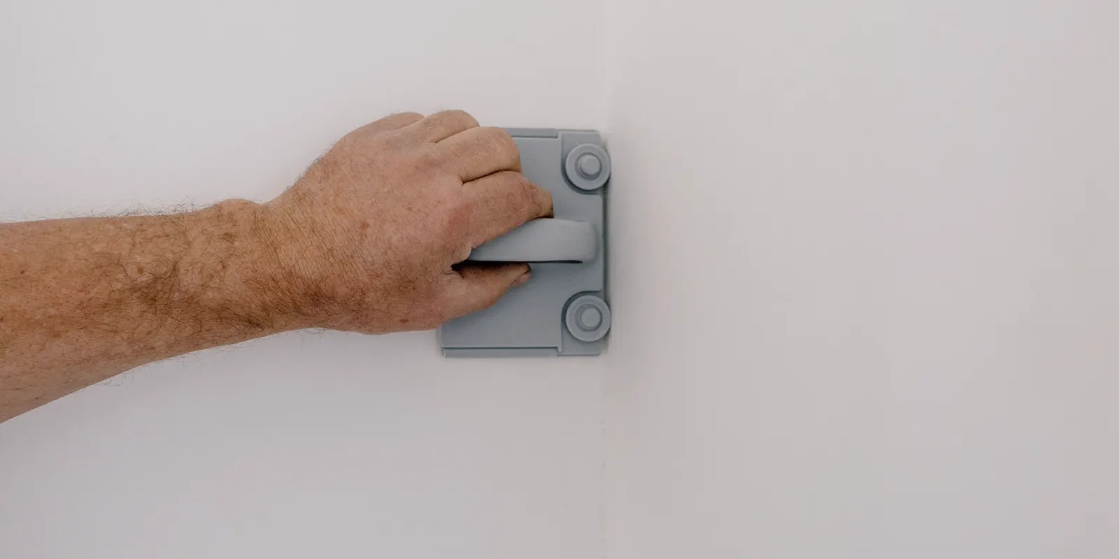 A worker's hands holding a scraper and sanding block, cabinet painting