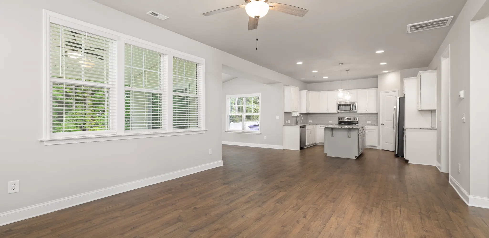 An empty living room with wood floors open to a white kitchen, home remodeling