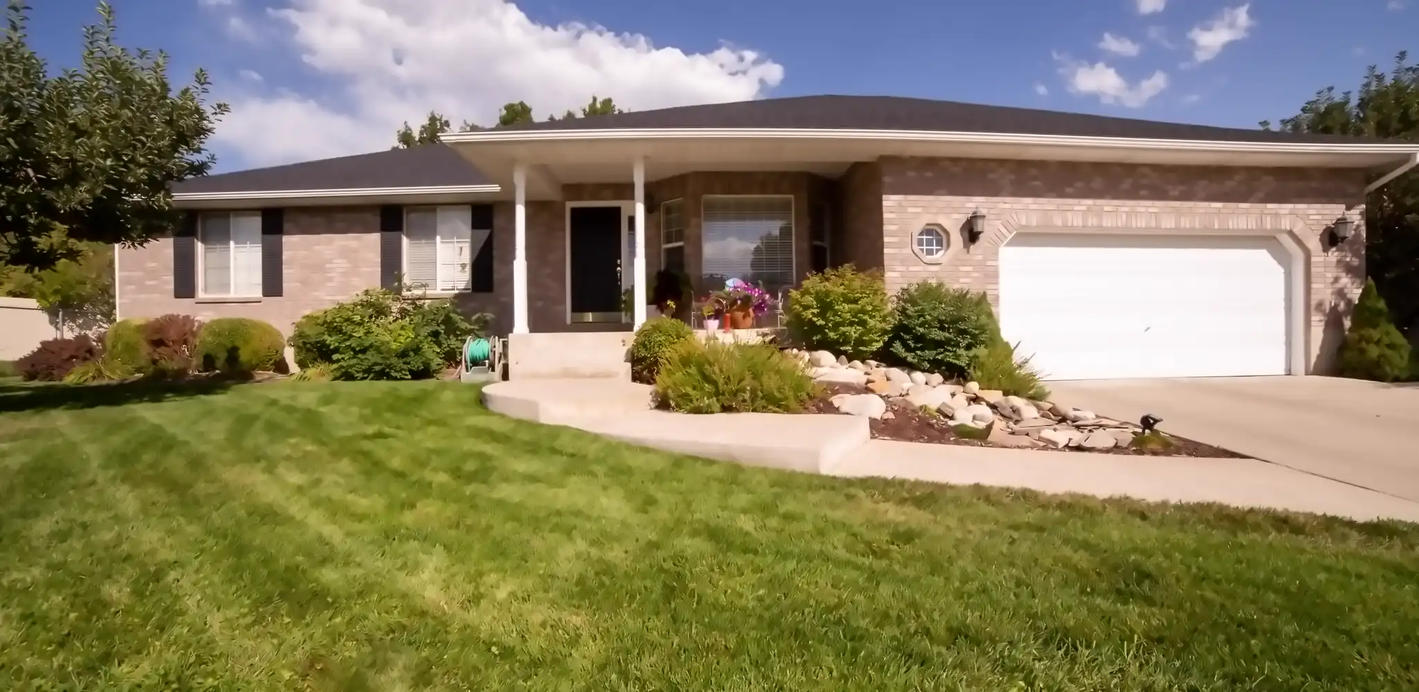 A house with a landscaped yard and a driveway on a sunny day, driveways