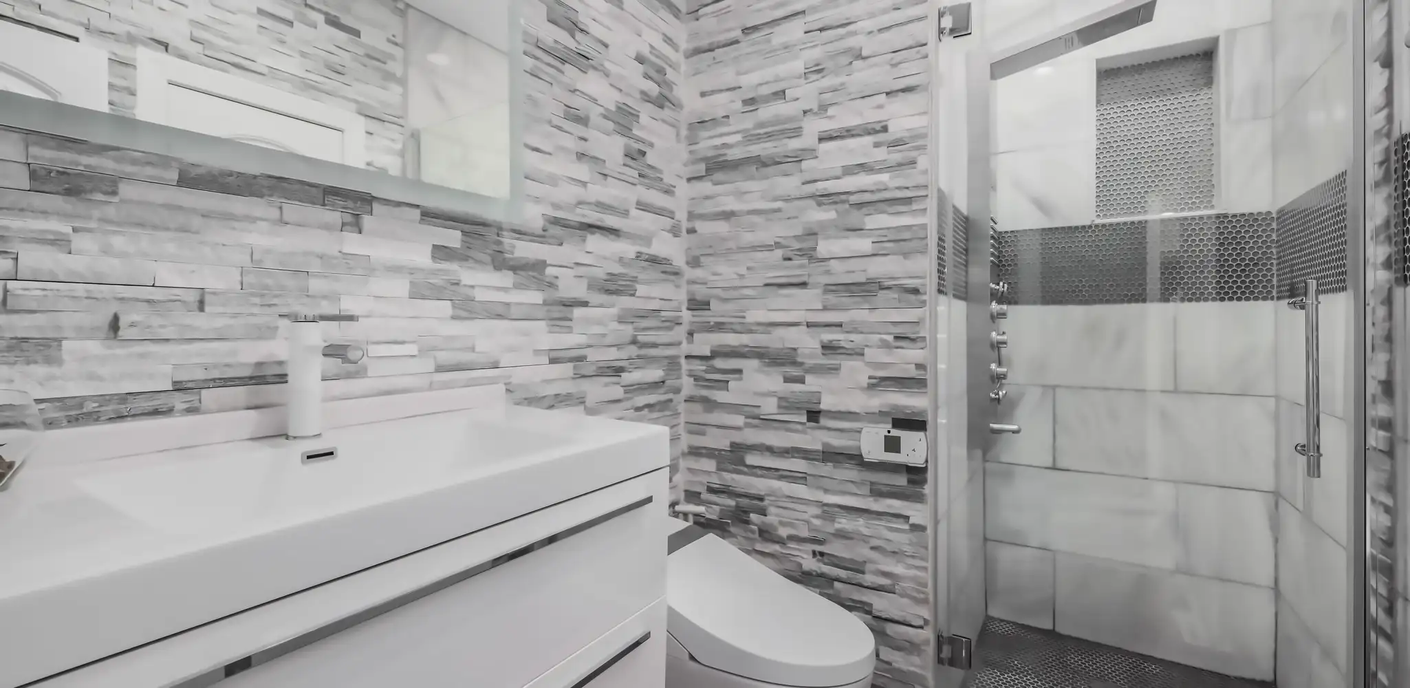 A glass shower with stone tile walls and a wood vanity, bathroom remodeling
