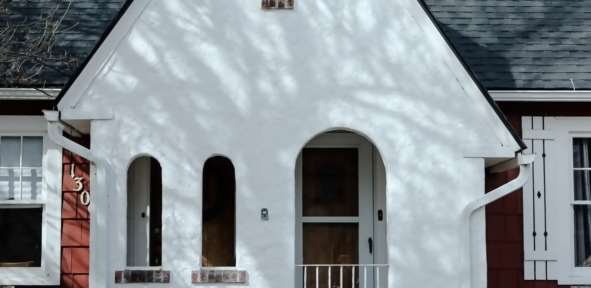 A white house with an arched entrance and a red door, exterior and front of house