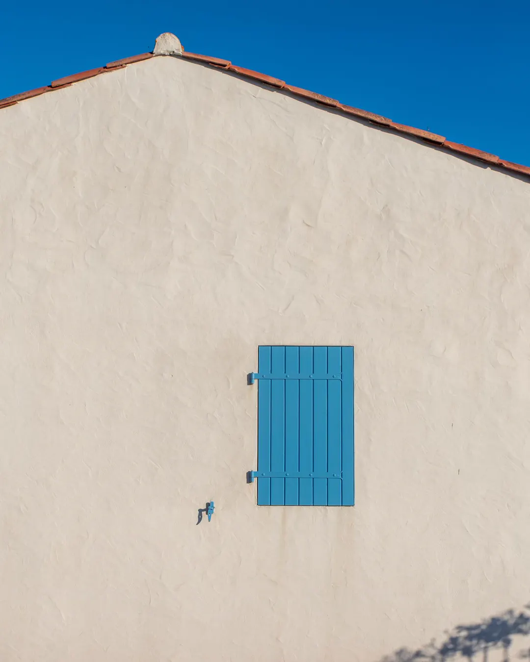 A white stucco wall with a blue shutter, exterior painting