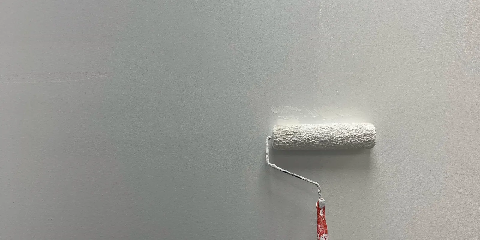A white wall partially painted with a roller, showing the patchy coverage, interior painting