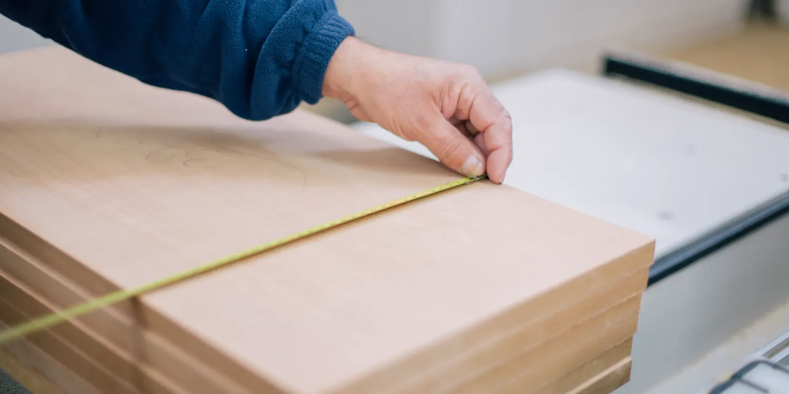 A carpenter's hand holding a tape measure on a wood surface, kitchen cabinet door replacement