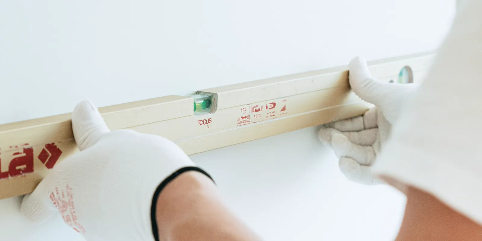 Hands in white gloves holding a spirit level against a wall, kitchen cabinet installation