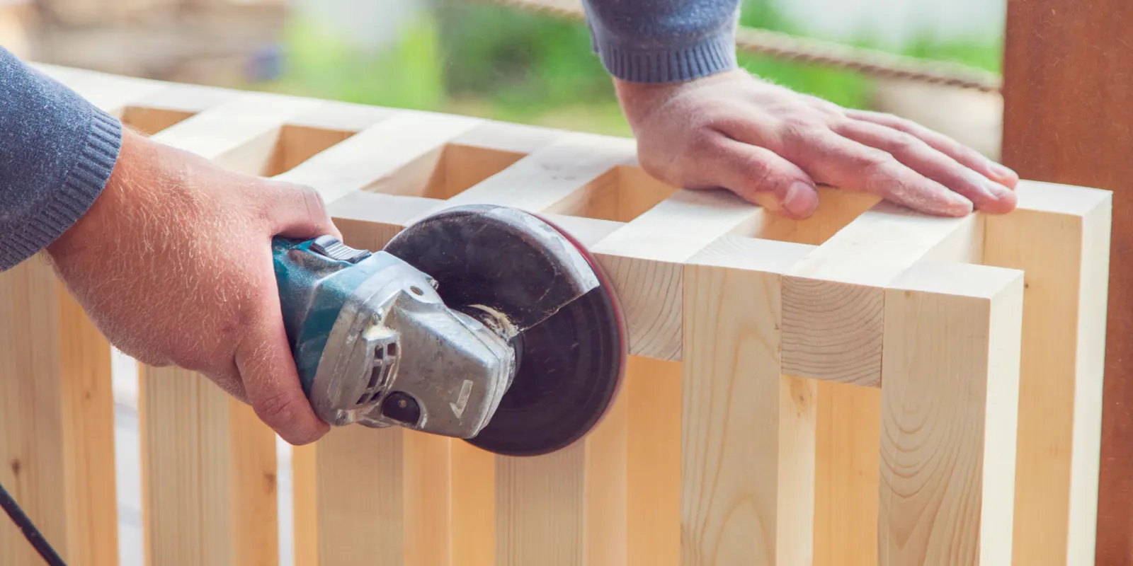 A woodworker seen from the side sanding a panel with an electric sander, kitchen cabinet refacing