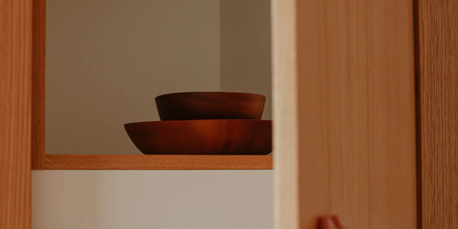 A hand opening a wooden kitchen cabinet door to show the box behind it, kitchen cabinet refacing