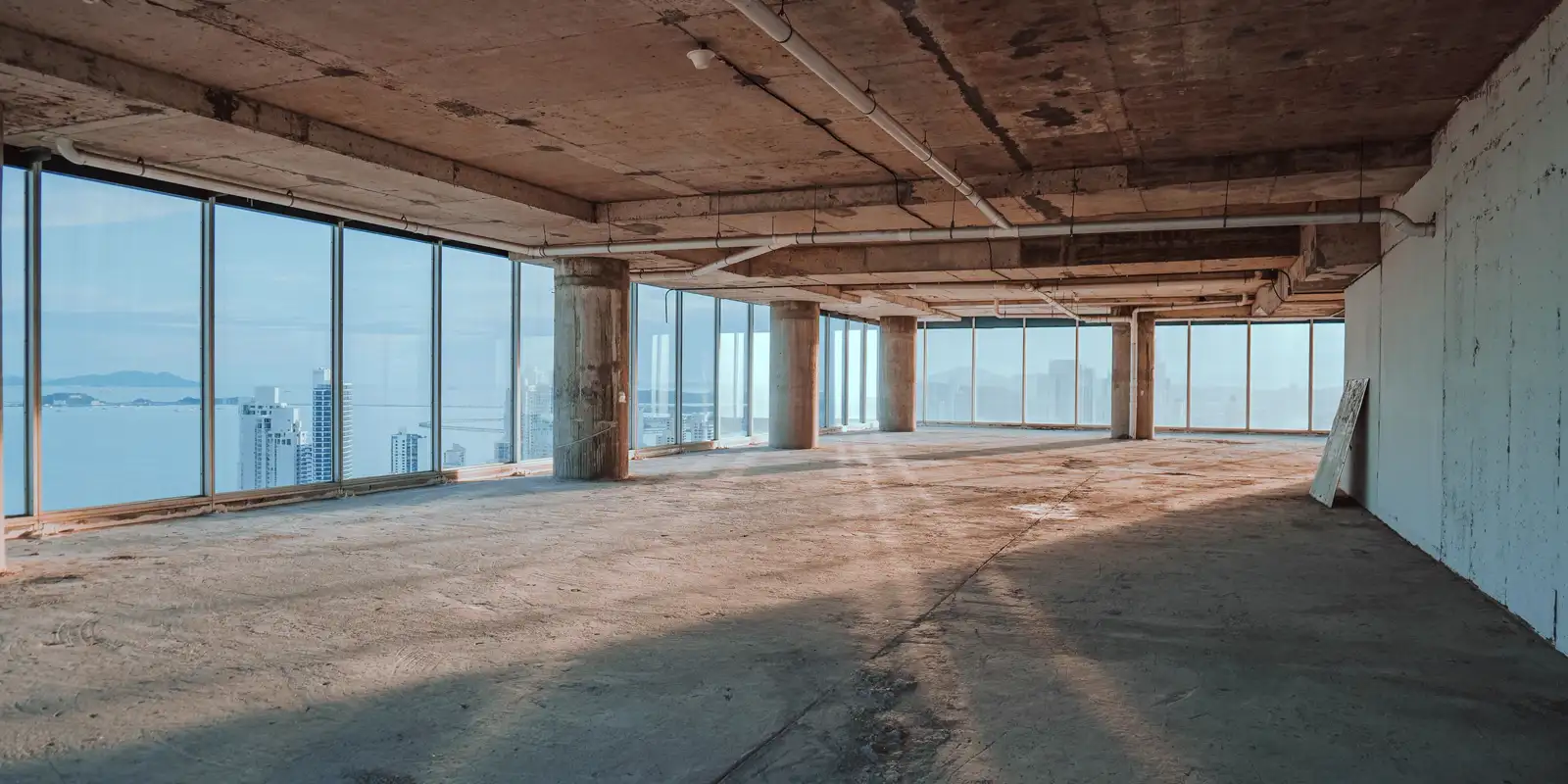A spacious empty interior with large windows and a bare concrete floor, luxury vinyl plank flooring