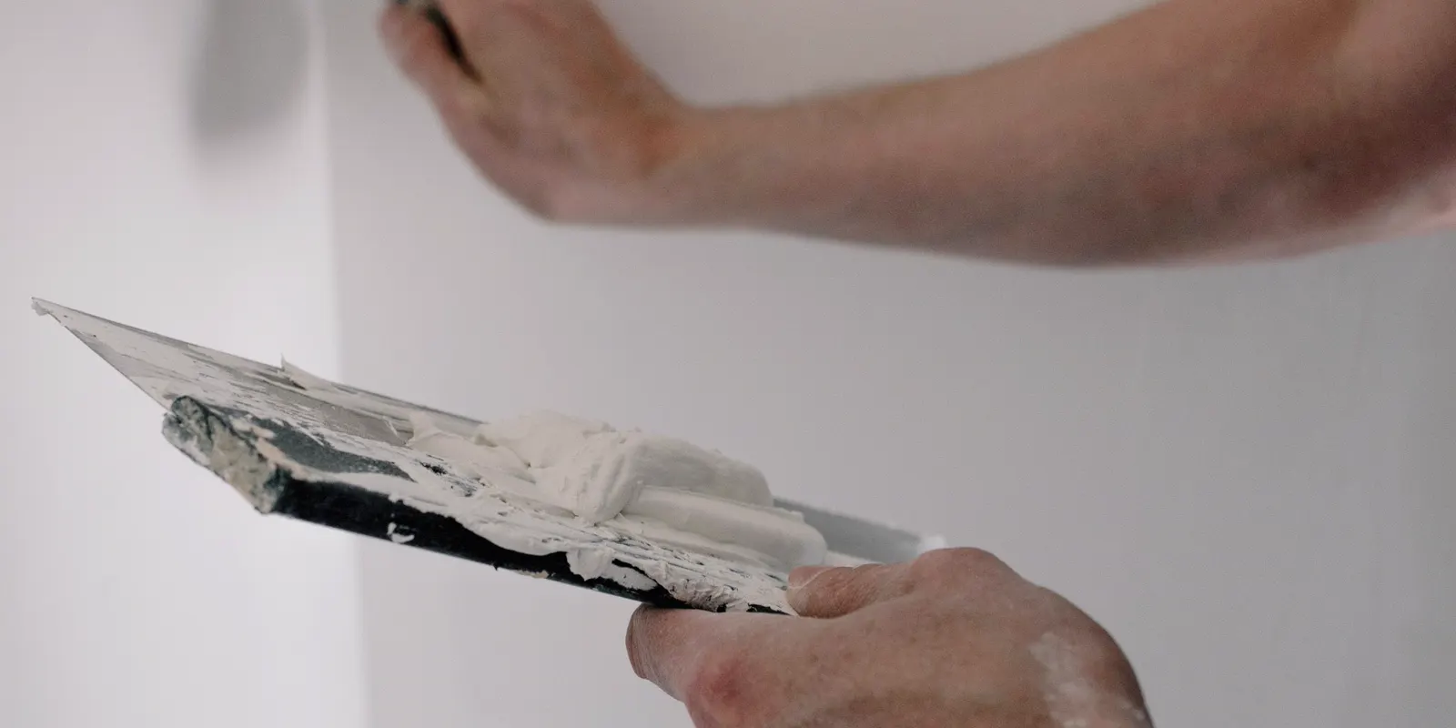 A worker's hands holding trowels with wall putty, painting cost