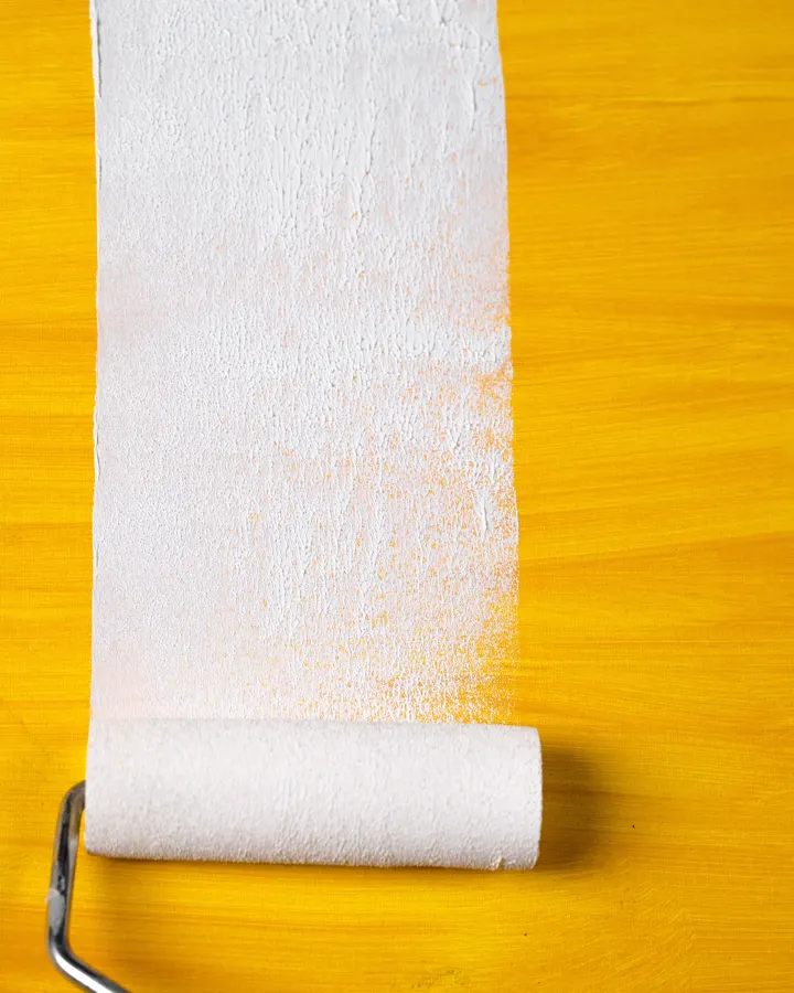 A paint roller leaving a white stripe over a yellow wall
