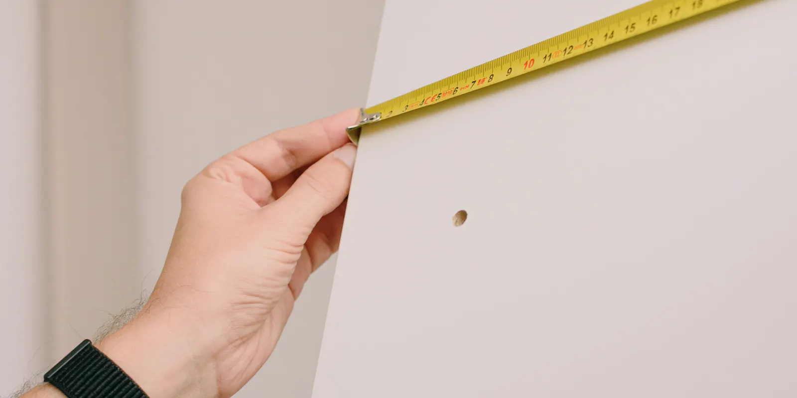 A hand holding a tape measure against a bare wall, small bathroom remodel