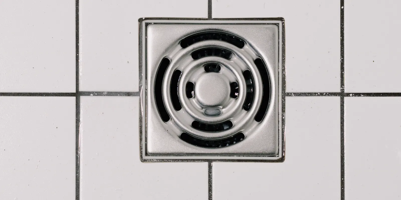 A white tile shower floor with the drain in the middle, tub to shower conversion